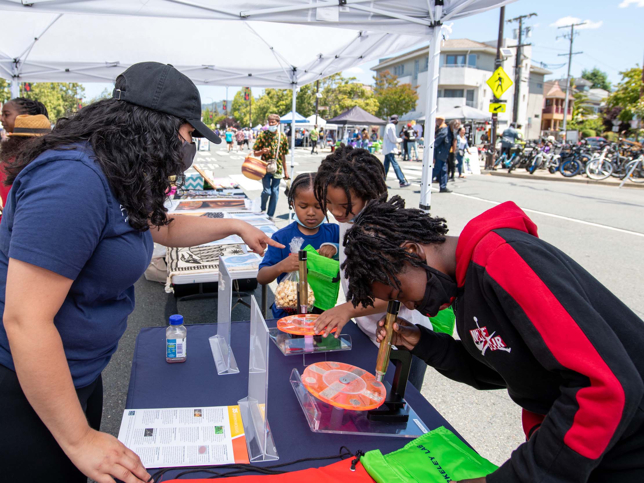 young person looks through microscope at a street fair booth while Berkeley Lab volunteer looks on
