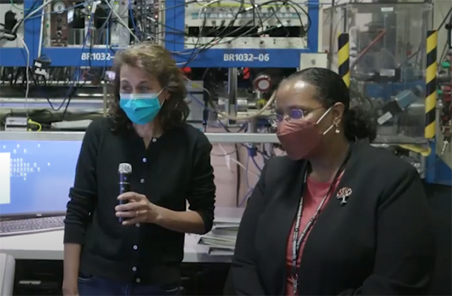DOE Office of Science Director Asmeret Berhe, a woman of color, stands in front of laboratory equipment with a Lab researcher, preparing to answer questions.