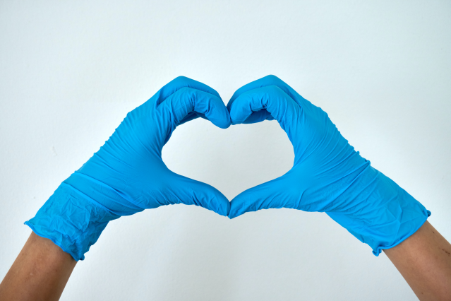 Hands wearing blue medical gloves forming heart with fingers.