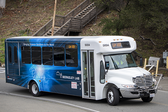 white and blue shuttle bus with dirt hillside behind