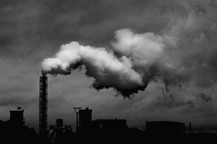 black and white image of smokestack again dark skyline