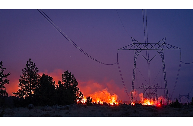 Fire at sunset burning near electrical power lines.
