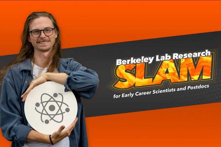 Researcher Emil Rofors holds an illustration of an atom while standing in front of the Berkeley Lab Research Lab SLAM logo