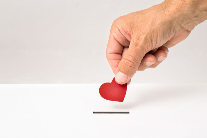 hand holding paper heart over a donation slot