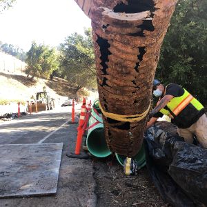a worker helps lift damaged storm drain pipe out of a trench