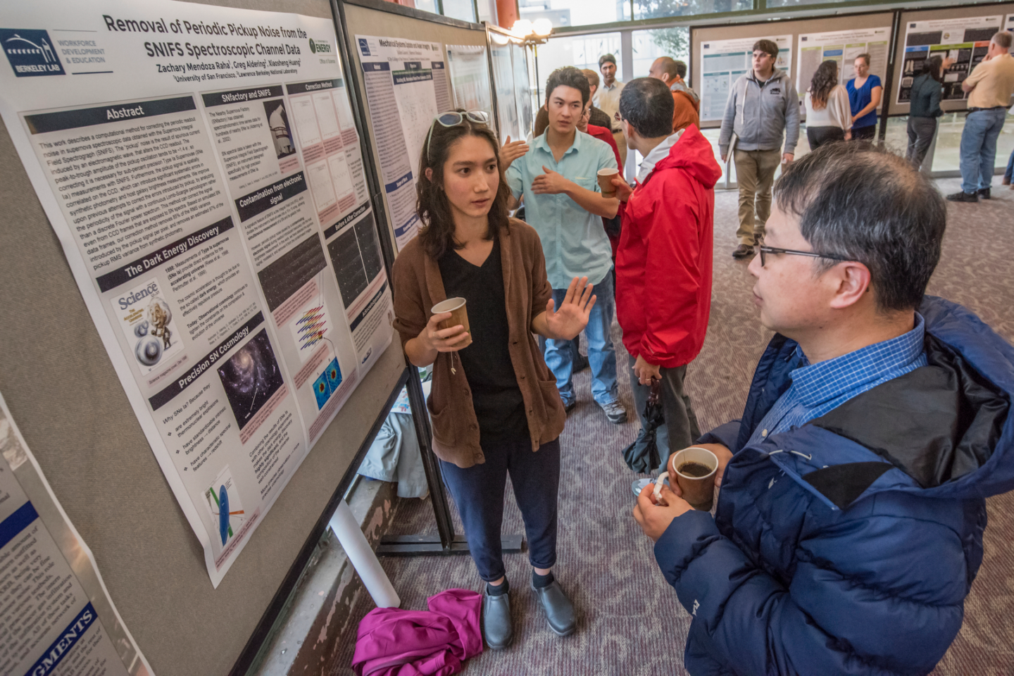 an intern explains her research to audience while standing in front of a poster detailing her work