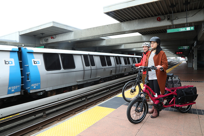 two people with bikes standing on BART platform with train in background