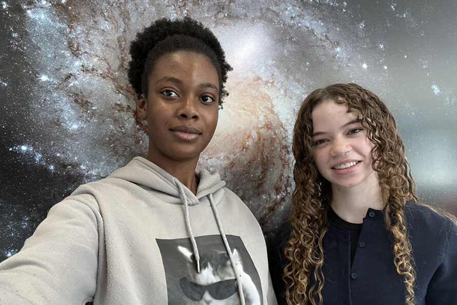 Two young persons standing in front of image of cosmos