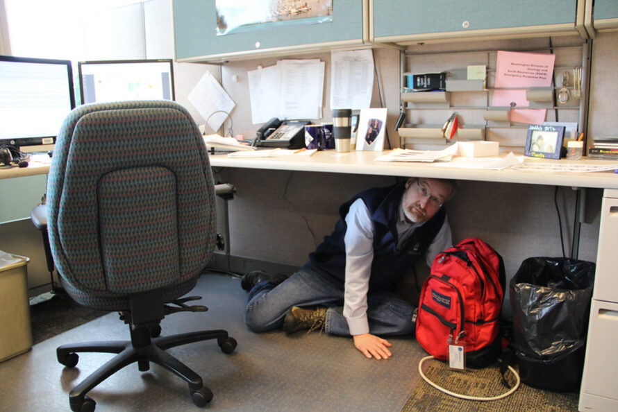 Photo of Washington state geologist Dave Norman does the "Drop Cover and Hold" exercise under his desk during an earthquake preparedness exercise.