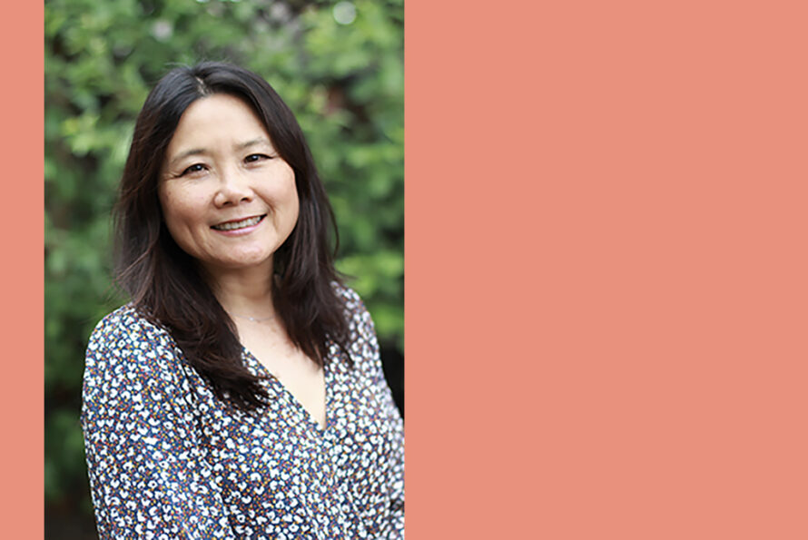 Person wearing a patterned shirt standing against green leafy background.