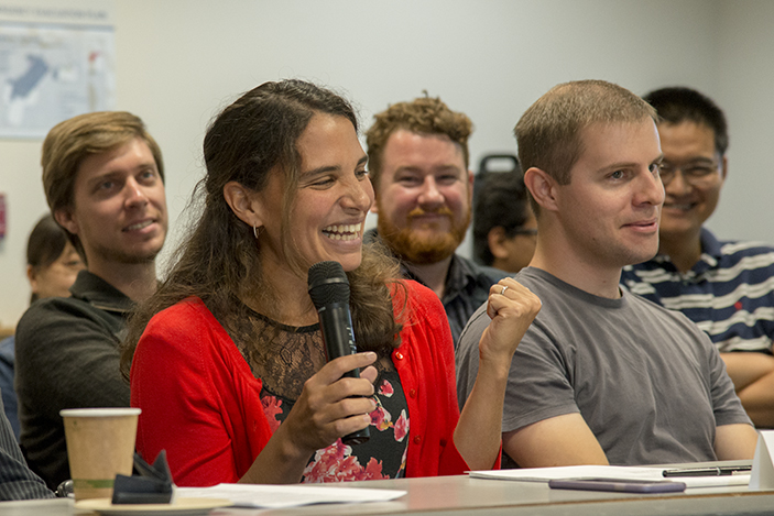 A group of seated persons with one person holding microphone