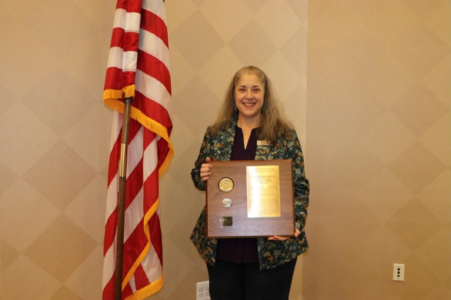 Person standing at podium displaying award plaque