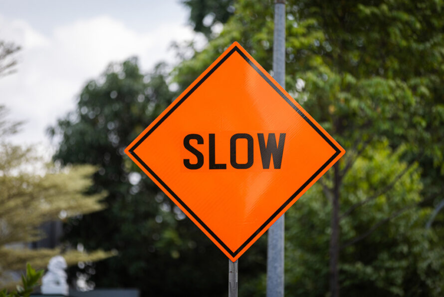 Orange diamond-shaped slow sign on a street with trees in the background.