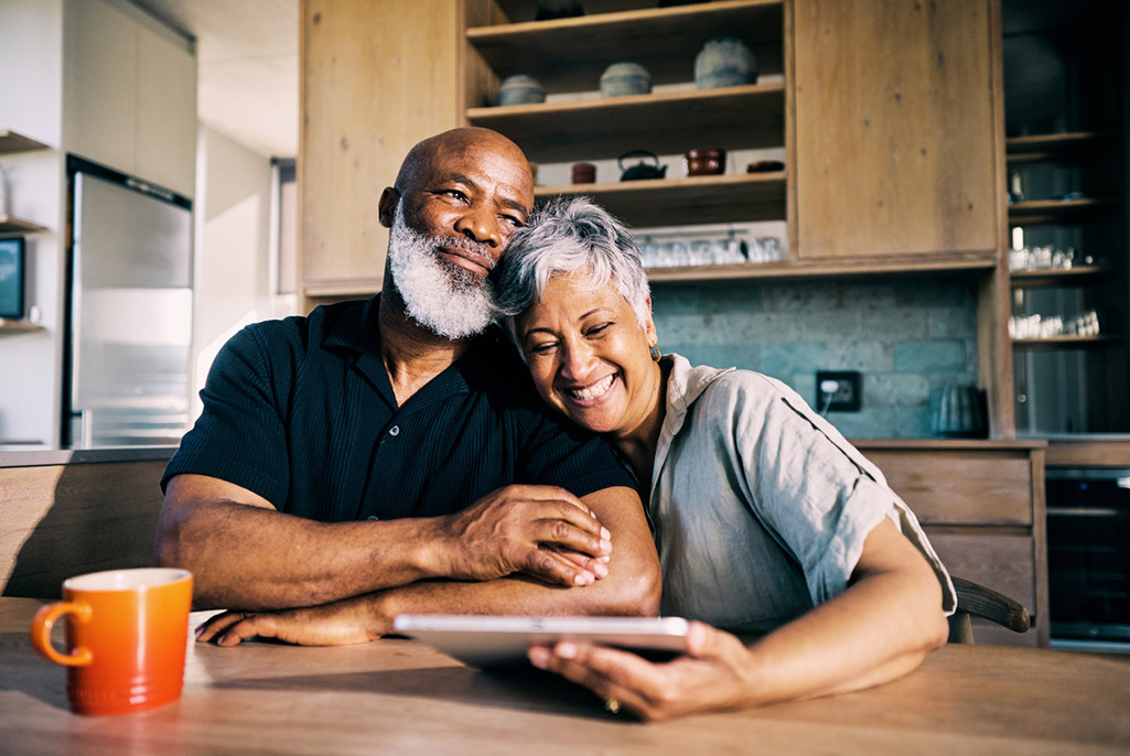Two people sitting at kitchen table with one holding tablet and both with intertwined hands