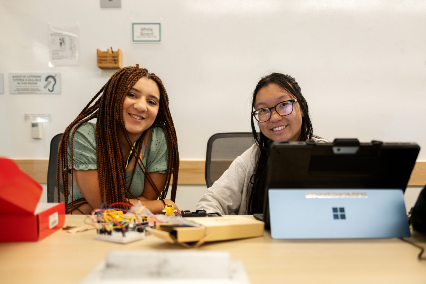 Two persons sitting at desk looking at laptop computer.