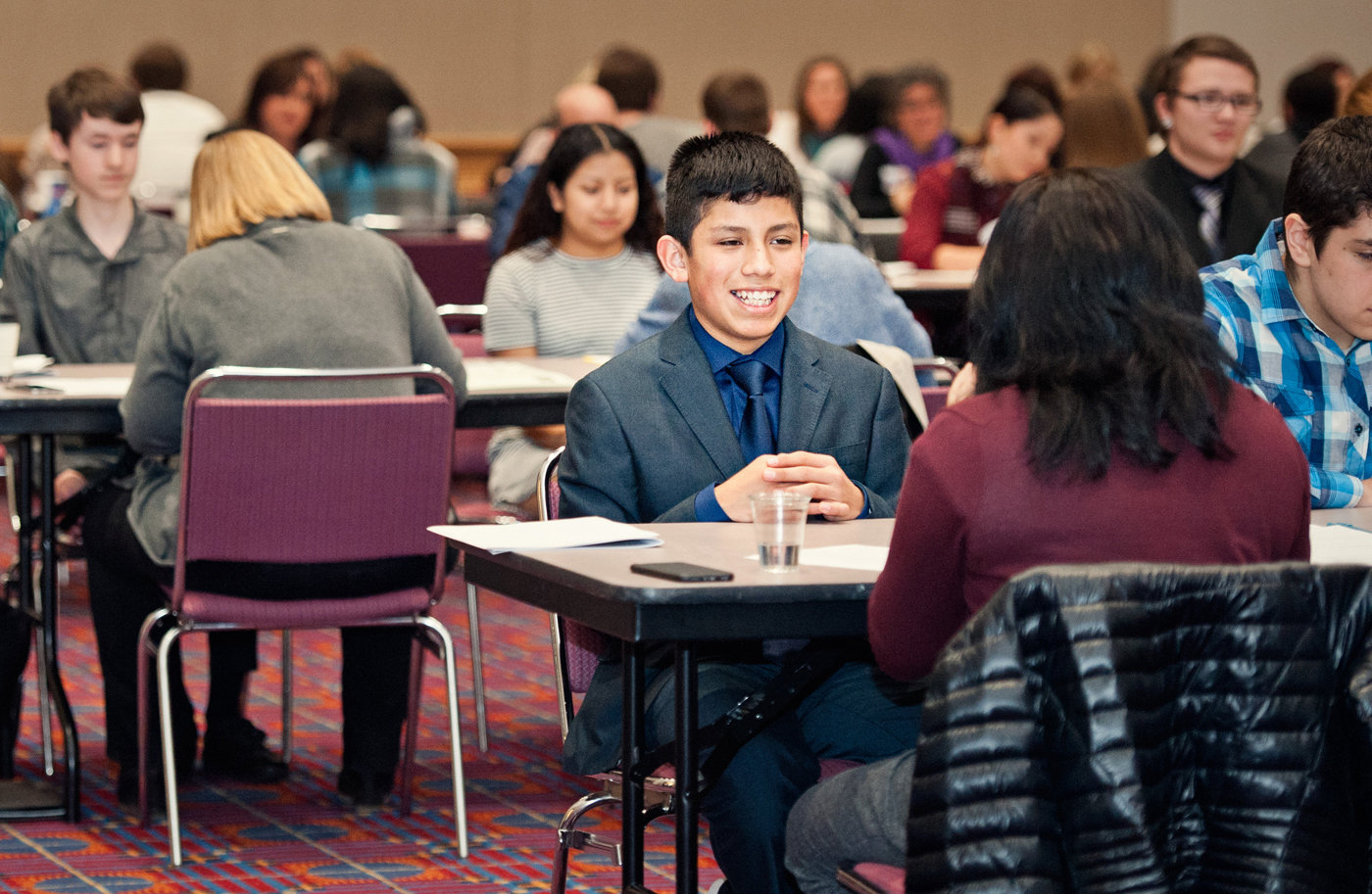 Young person wearing suit sitting across from person interviewing them.