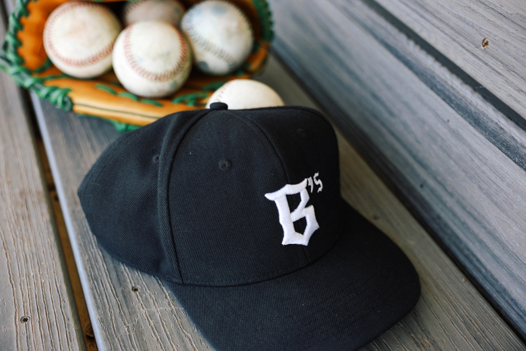 Close-in shot of baseball cap and glove with balls sitting on a bench.
