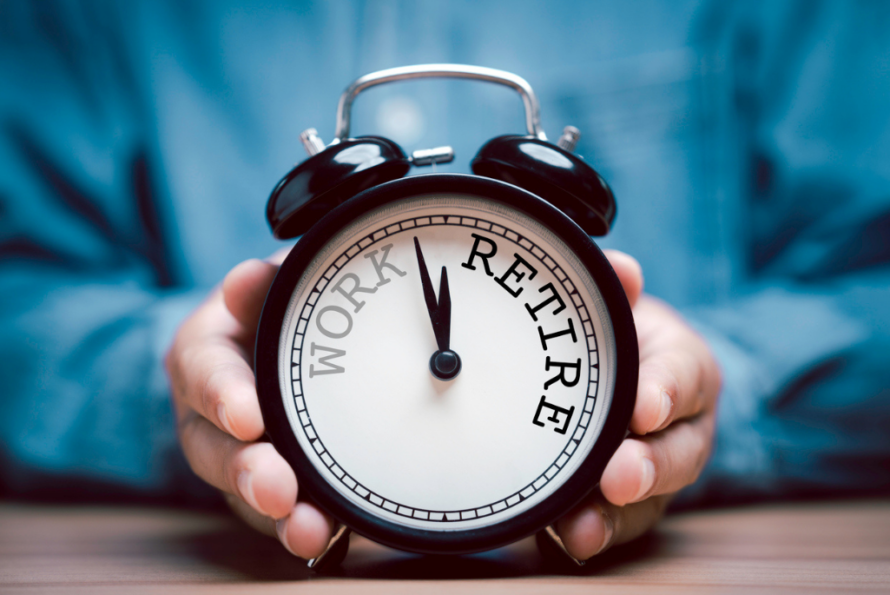 Hands hold an alarm clock with the words "work' and "retire" printed on the clockface.