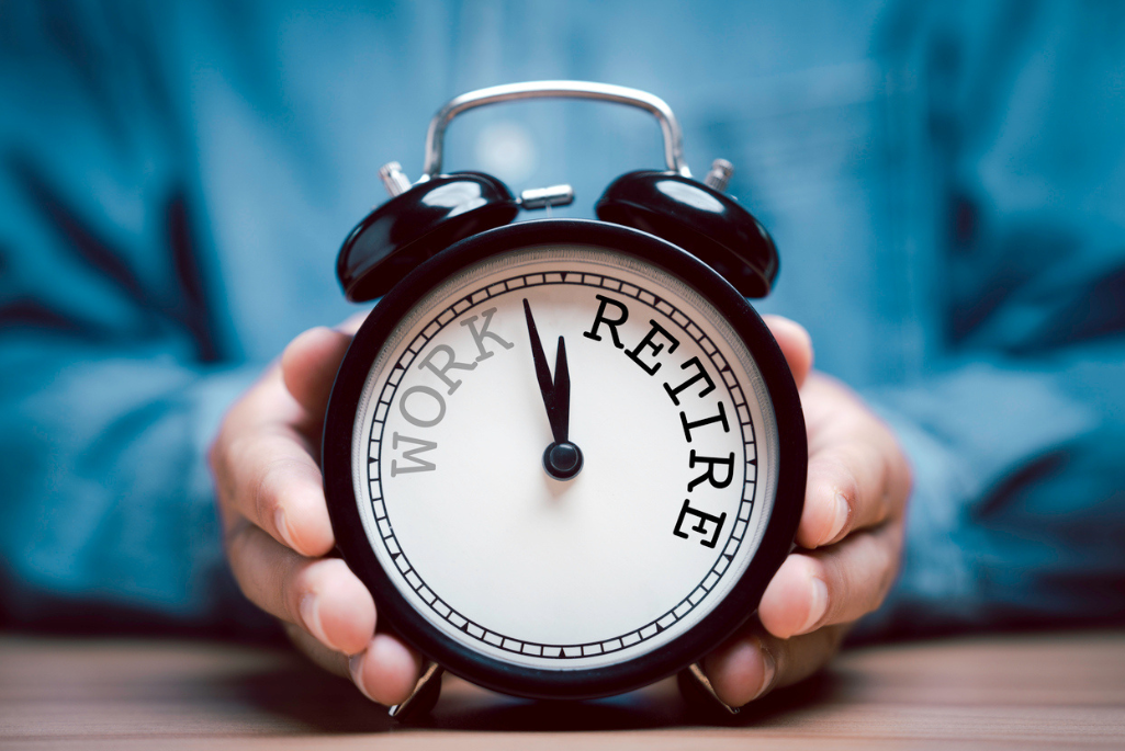 Hands hold an alarm clock with the words "work' and "retire" printed on the clockface.
