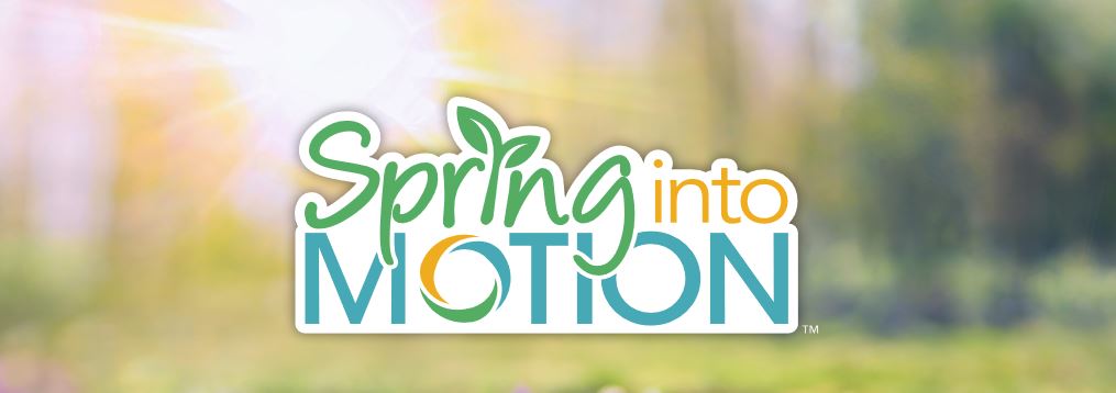 Blurred background of sun shining with trees and greenery. Text in front reads, Spring into Motion.