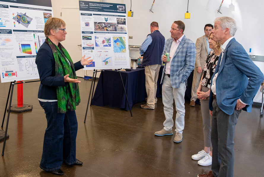 Person wearing dark jacket and pants standing in front of poster explaining details from poster to group of people