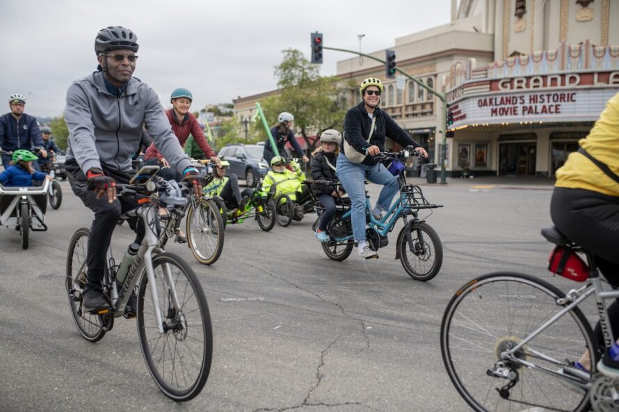 A group of cyclists wearing bike helmets ride along the streets of Oakland.