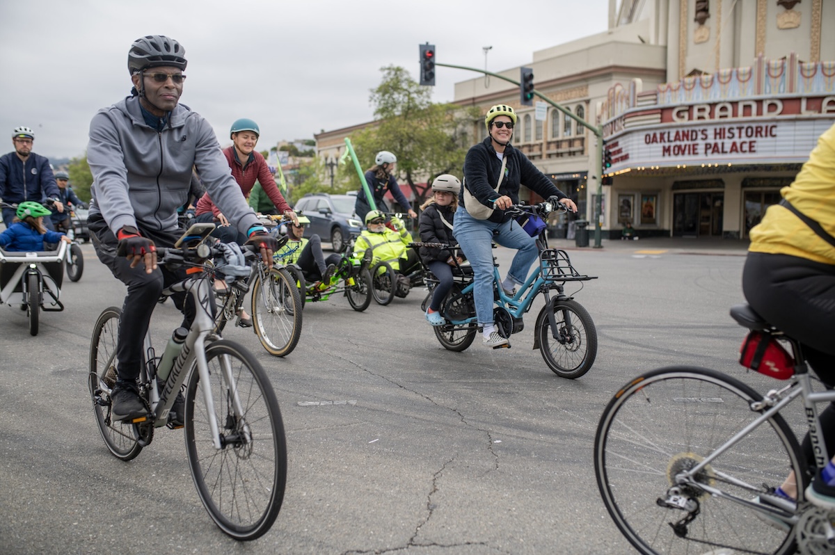 A group of cyclists wearing bike helmets ride along the streets of Oakland.