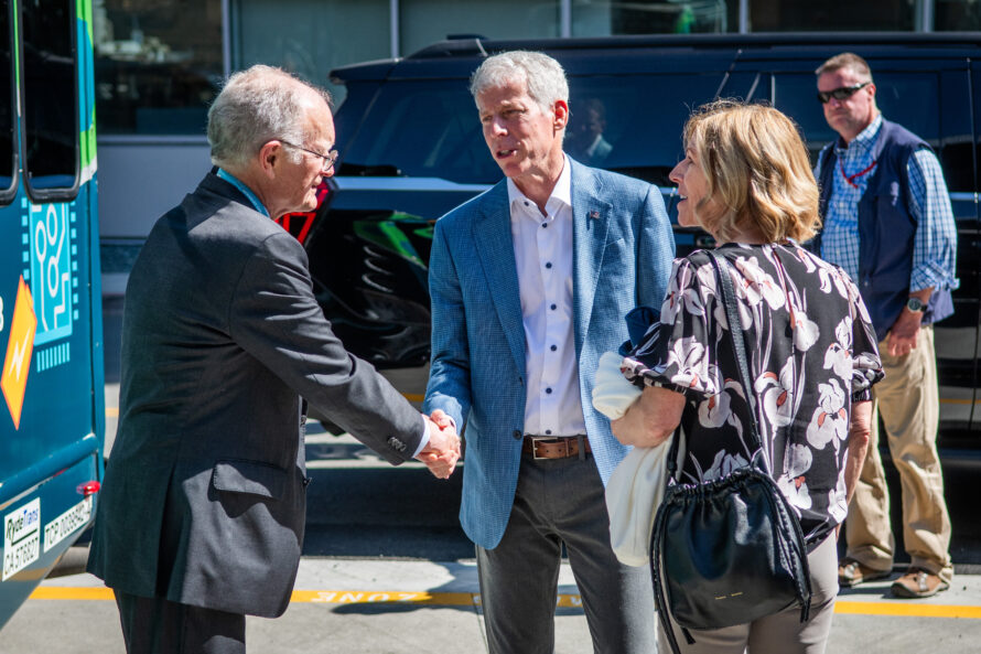 Person in dark suit shaking hands with person in jacket while others look on.