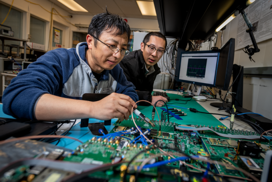 Person making adjustment to green circuit board with another person looking on.