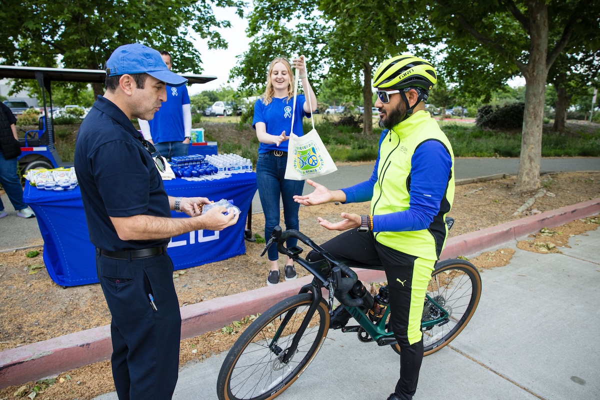 A cyclist clad in biking gear receives swag from a volunteer at an energizer booth.