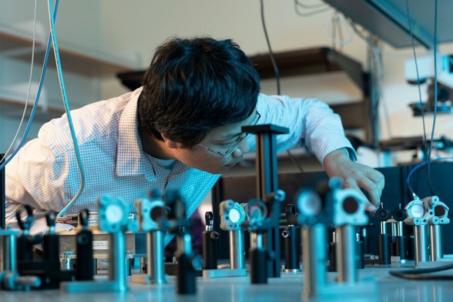 Person in lab coat examining scientific device on a table.