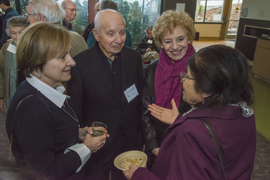 Gathering of persons talking amongst themselves while holding plates of food and drinks.