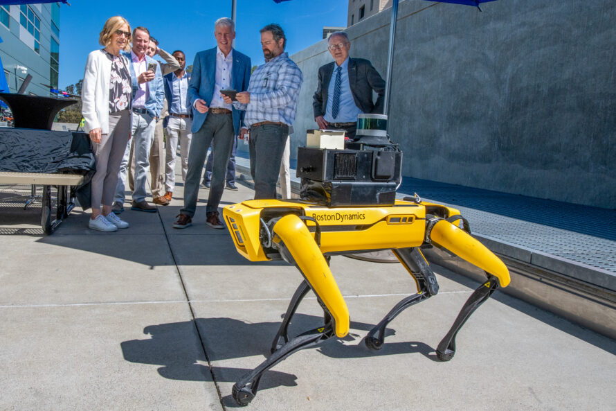 Yellow robot dog in foreground with group of people watching it operating in background