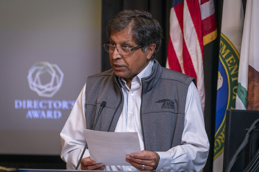 Person wearing light blue shirt and gray vest standing at podium holding note cards and giving speech