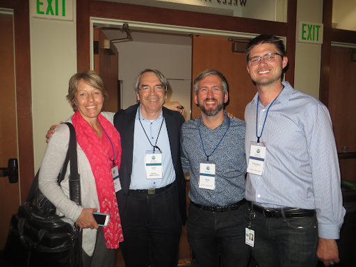 Four persons wearing lanyards and standing inside room.
