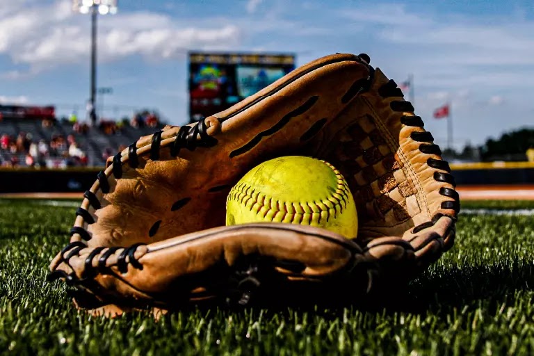 Closeup of baseball mitt with softball resting inside all on baseball field.