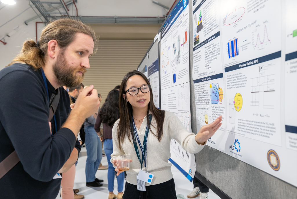 Two persons involved in a science poster session standing in front of poster with one person gesturing toward poster.