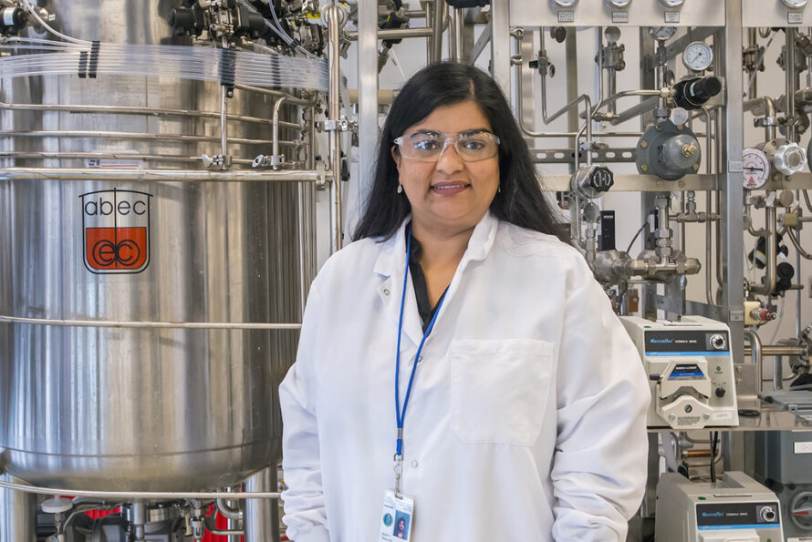 Person wearing a white lab coat and safety glasses standing in front of biologic processing vat