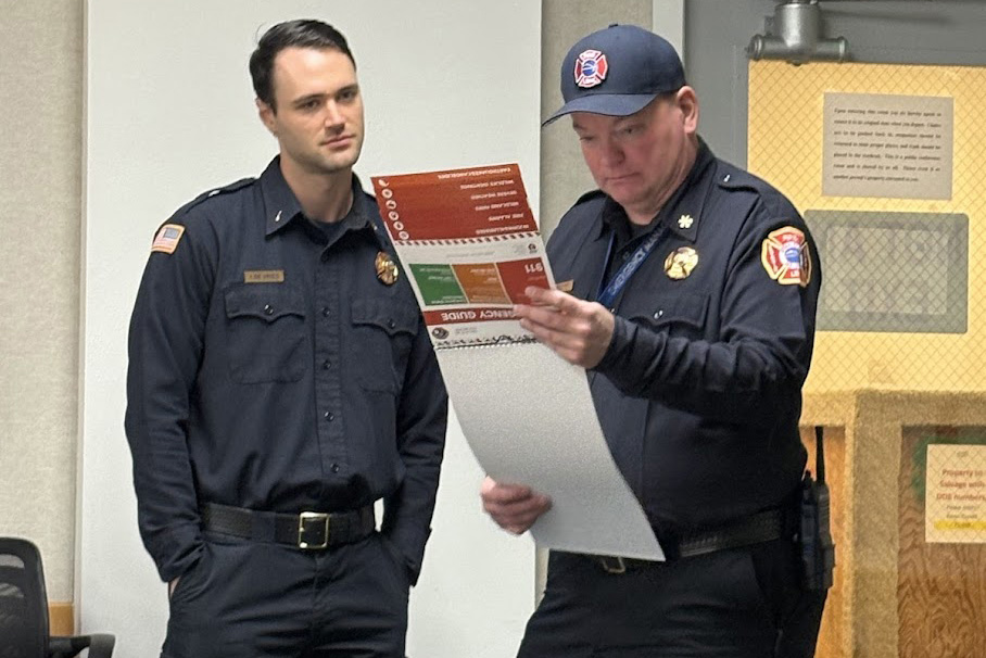 Two people both in fire inspector uniforms are reviewing a spiral booklet with a bright red cover.