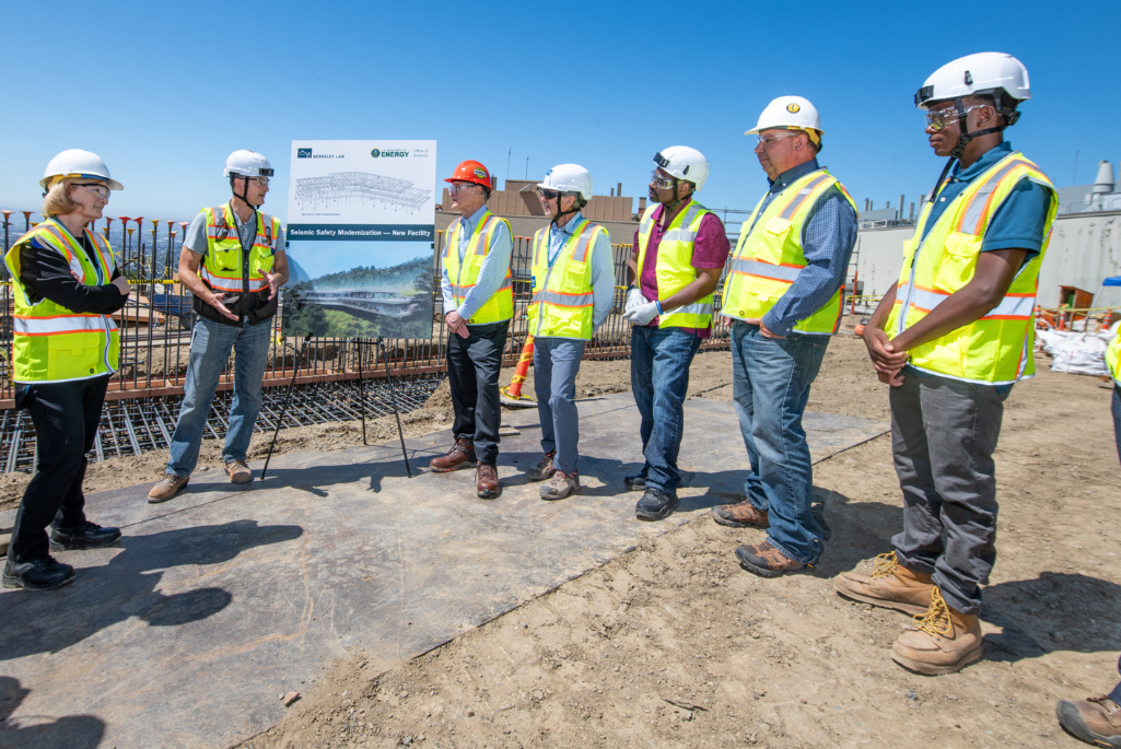 A group of people in hard hats and safety vests stands on a construction site