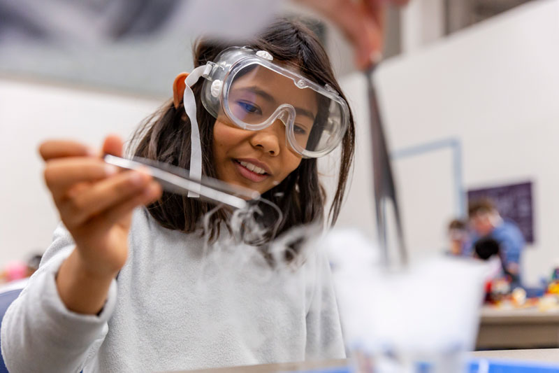 Person in lab protective equipment placing a device into a solution.