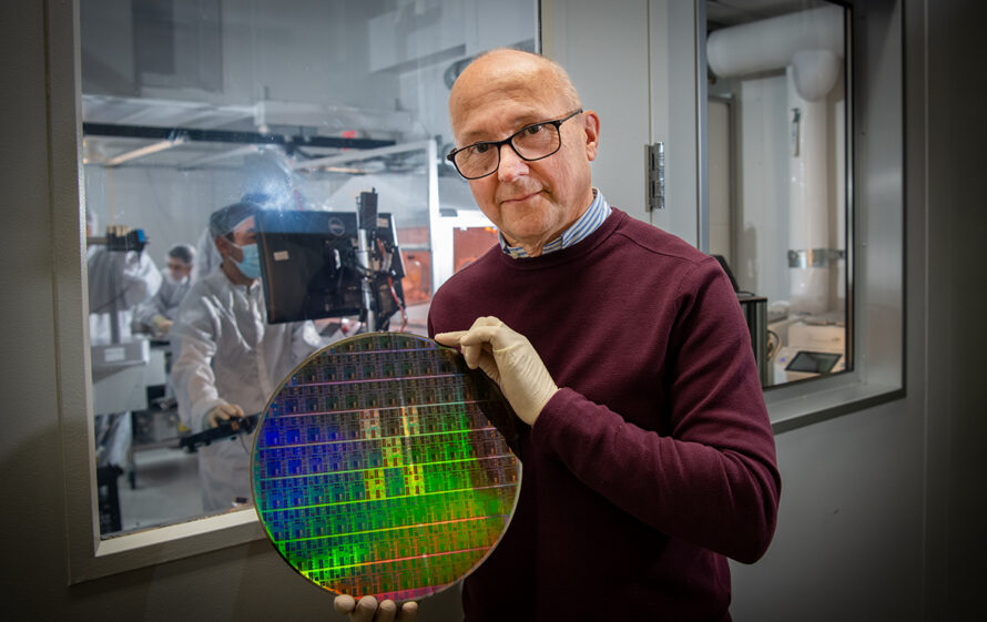 Person wearing dark red long sleeve sweater holding a large colored microchip with scientific lab in the background