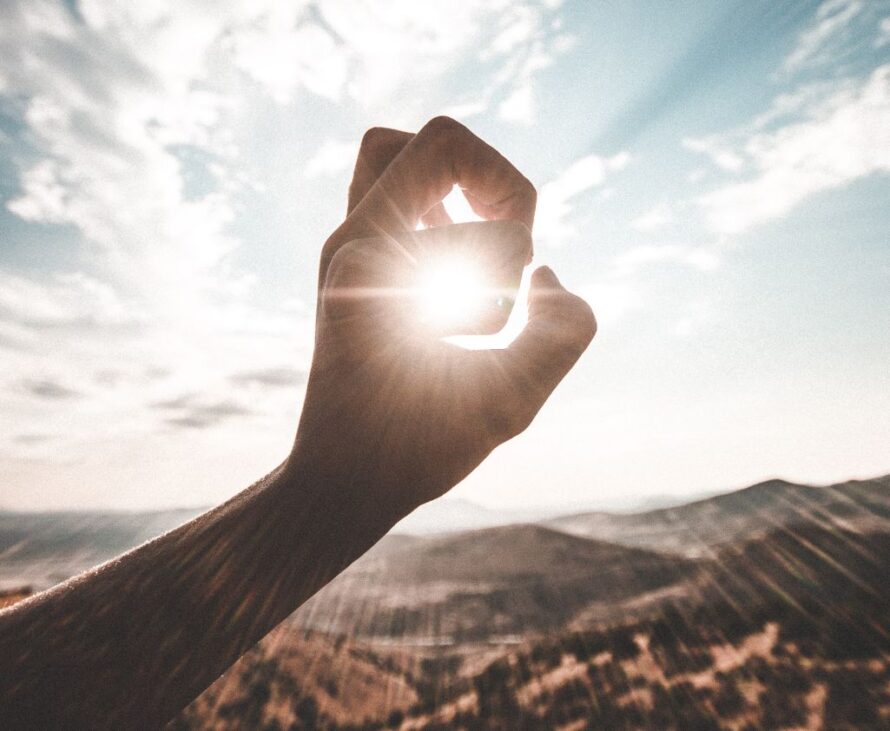 Closeup of person's hand held up to sun with sun rays shining through and illuminating hand.