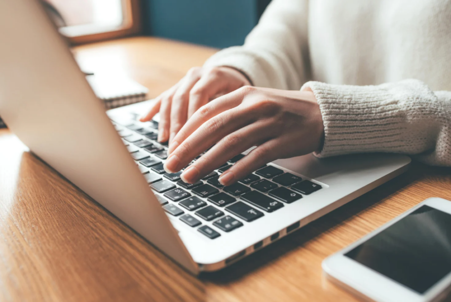 Closeup of person typing on laptop computer sitting on desk.