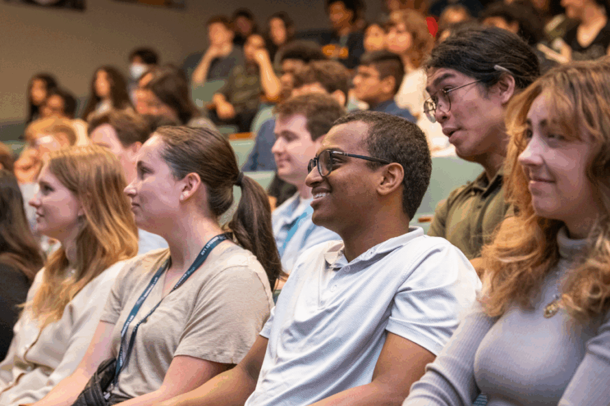 Large gathering of persons seated in auditorium watching presentation.