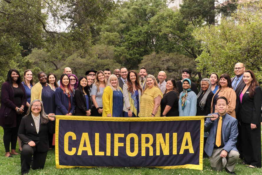 Group of persons standing together holding brown banner with yellow word "California".