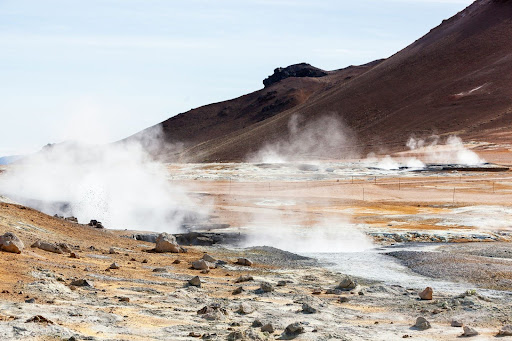 Barren landscape with geothermal steam rising from ground in several places.
