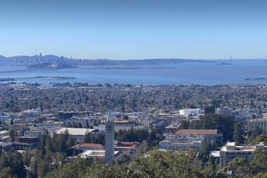 View from a hillside that includes bay water, a city at the end of a bridge, and another bridge spanning entrance to bay,