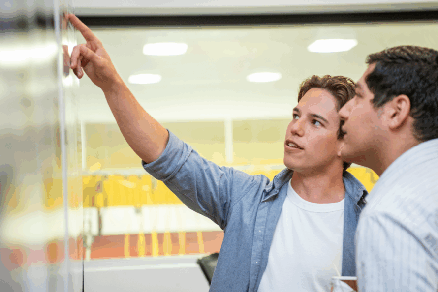 Twp persons in a room looking at a poster with one person pointing to something.