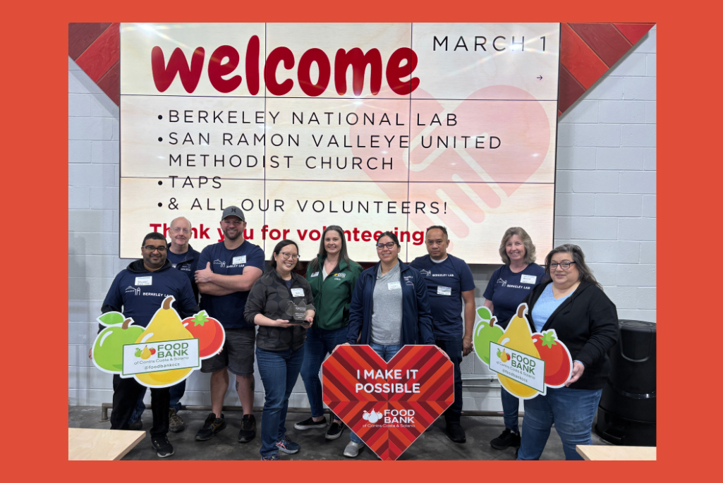 Group of persons standing in front of a large poster with the word "Welcome".